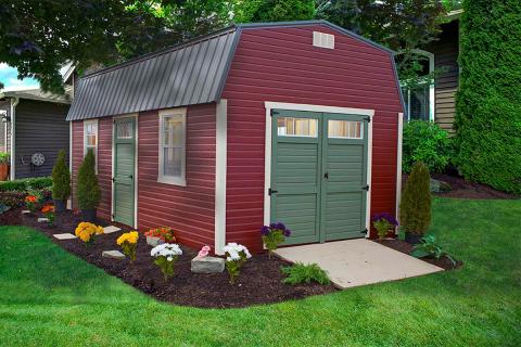 High barn with red siding, white trim, green double doors, windows, a green single door, and a metal roof sitting in a backyard.